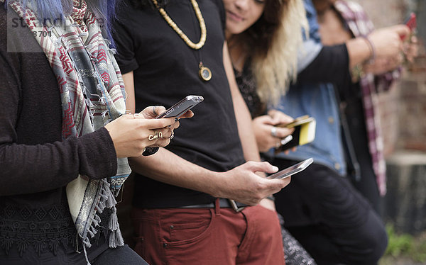 Junge Menschen stehen in einer Reihe und benutzen Smartphones