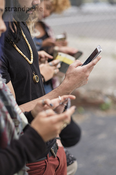 Junge Menschen stehen in einer Reihe und benutzen Smartphones