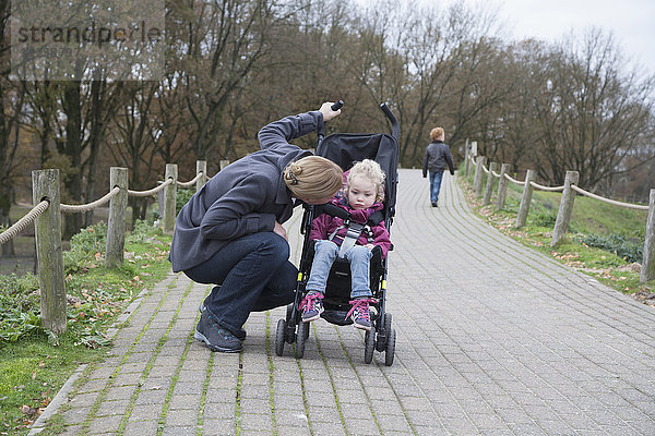 Mutter spricht mit Tochter (4-5)  die im Kinderwagen sitzt  Junge (8-9) läuft im Hintergrund