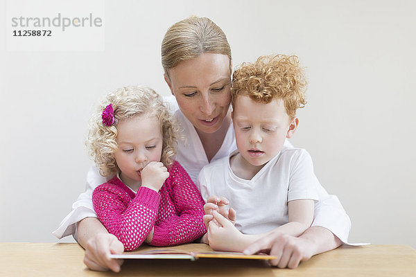 Mutter liest Sohn (8-9) und Tochter (4-5) ein Buch vor