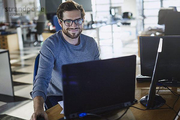 Porträt eines lächelnden Geschäftsmannes  der am Computer im Büro arbeitet