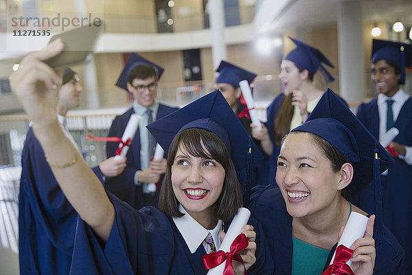 College-Frauen Absolventinnen in Mütze und Kittel nehmen Selfie mit Diplomen