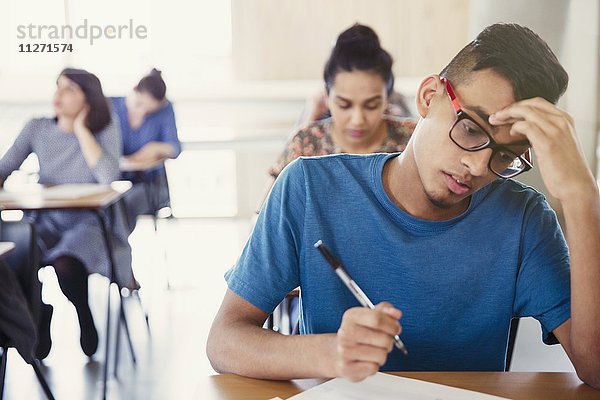 Ernste männliche Studentin beim Test am Schreibtisch im Klassenzimmer