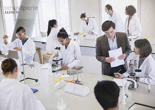 Wissenschaftsprofessor und Studenten mit Mikroskopen im naturwissenschaftlichen Laborunterricht