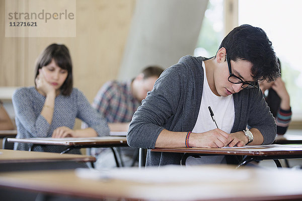 Fokussierter männlicher Student beim Test am Schreibtisch im Klassenzimmer