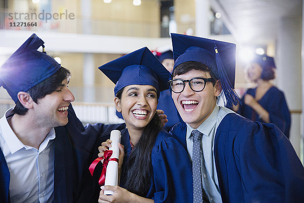 Glückliche Hochschulabsolventen in Mütze und Kleid feiern mit Diplom
