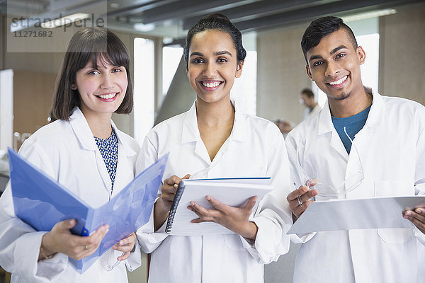 Portrait lächelnde Studenten in Laborkitteln mit Notizbüchern im Klassenzimmer des Wissenschaftslabors