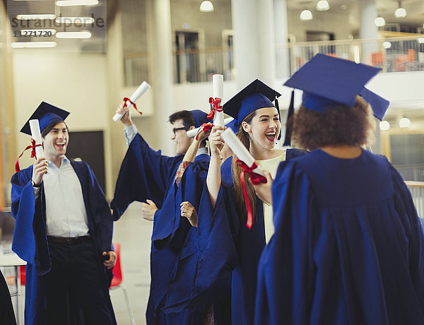 Hochschulabsolventen in Mütze und Kittel mit Diplomen