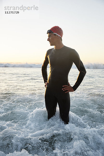 Triathlet im Neoprenanzug stehend in der Meeresbrandung