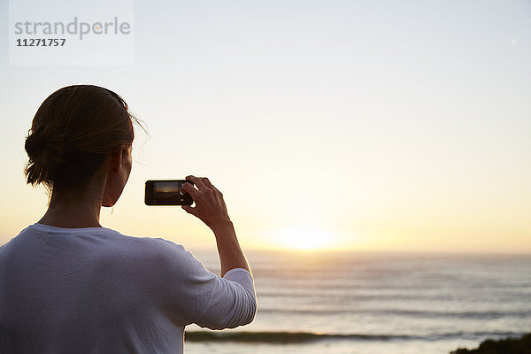 Frau fotografiert Sonnenuntergang über dem Meer mit Fotohandy