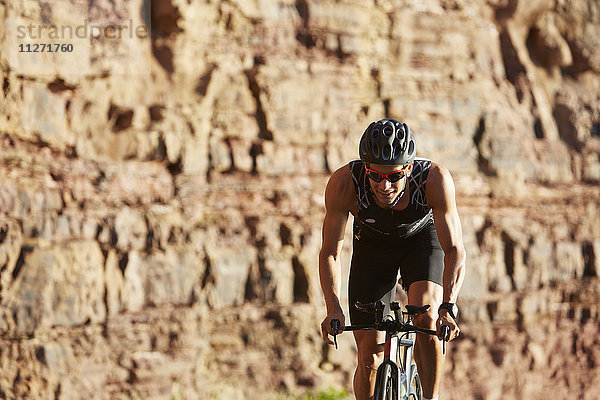 Männlicher Triathlet mit dem Fahrrad auf sonnigen Felsen