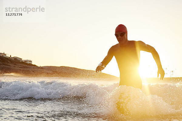 Triathletenschwimmer im Neoprenanzug  der aus dem sonnigen Meer läuft