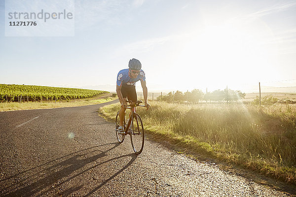 Männlicher Triathlet Radfahrer auf sonniger Landstraße bei Sonnenaufgang
