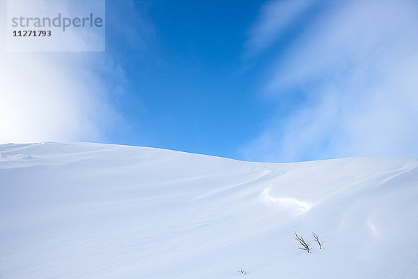 Schneebedeckter Hügel unter blauem Himmel