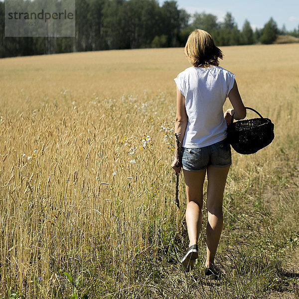 Kaukasische Frau geht mit Korb und Stock durch ein Feld