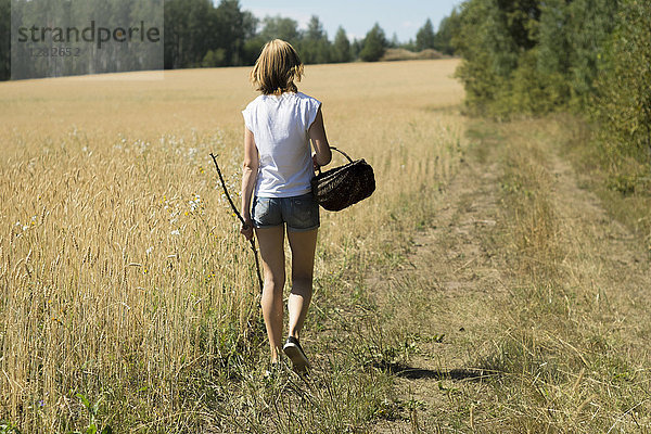 Kaukasische Frau geht mit Korb und Stock durch ein Feld