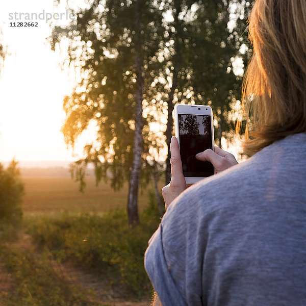 Kaukasische Frau fotografiert Sonnenuntergang mit Mobiltelefon