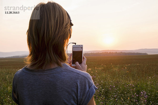 Kaukasische Frau fotografiert Sonnenuntergang mit Mobiltelefon
