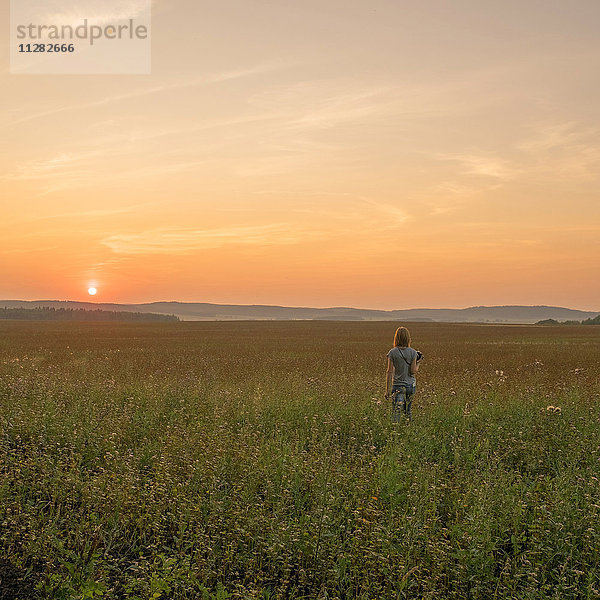 Kaukasische Frau  die bei Sonnenuntergang in einem Feld spazieren geht