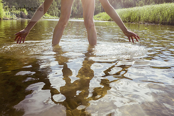 Beine und Arme einer in einem Fluss watenden kaukasischen Frau