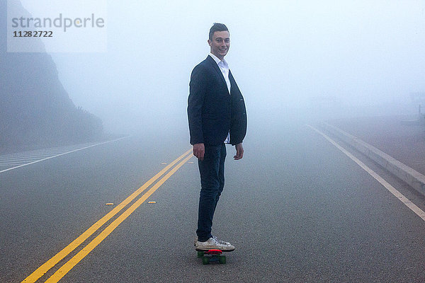 Kaukasischer Mann steht auf kleinem roten Skateboard im Nebel