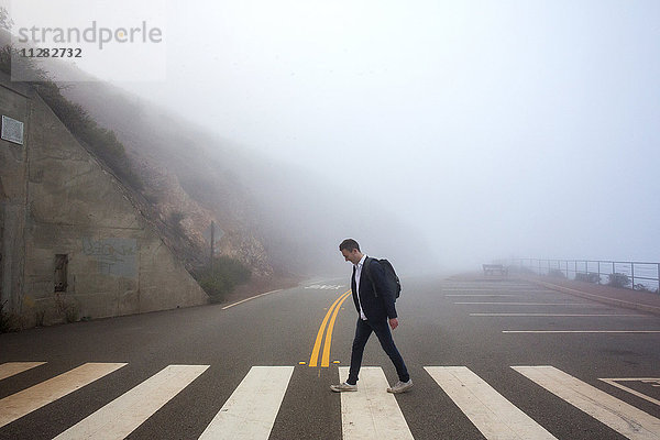 Kaukasischer Mann geht bei Nebel über einen Zebrastreifen