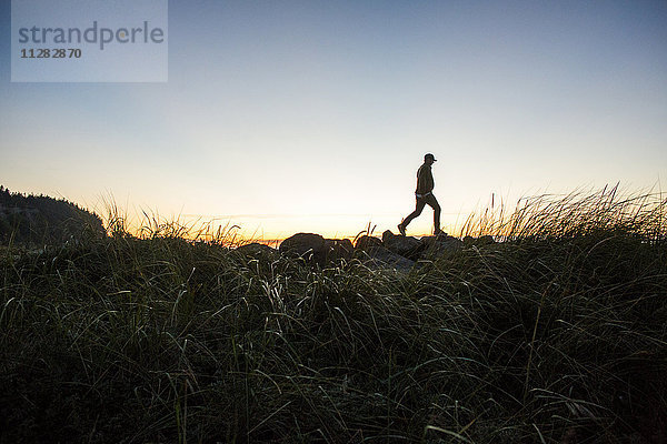 Silhouette eines fernen kaukasischen Mannes  der bei Sonnenuntergang auf einem Felsen spazieren geht