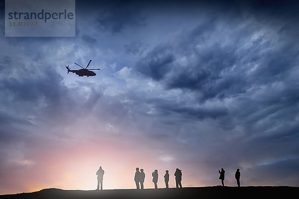 Silhouette eines Hubschraubers  der bei Sonnenuntergang über Menschen fliegt