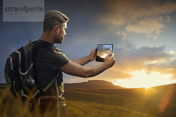 Kaukasischer Wanderer fotografiert Sonnenuntergang mit digitalem Tablet