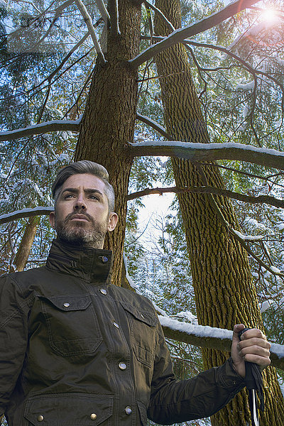 Kaukasischer Wanderer hält Wanderstock unter verschneitem Baum