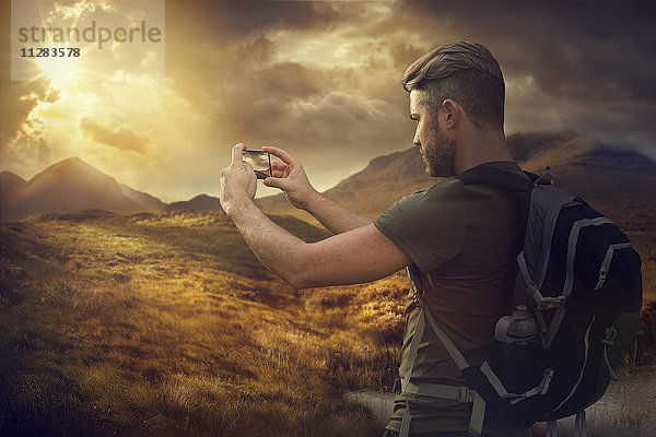 Kaukasischer Wanderer  der mit seinem Handy den Sonnenuntergang in den Bergen fotografiert