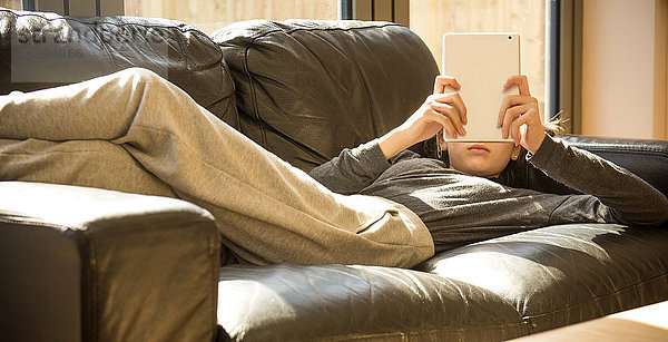 Mädchen liegt auf dem Sofa und liest auf einem digitalen Tablet