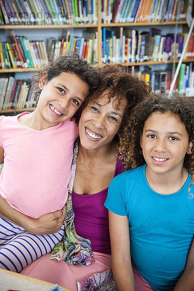 Lächelnde Mutter posiert mit Töchtern in der Bibliothek