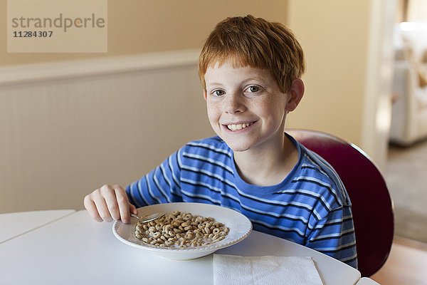 Lächelnder kaukasischer Junge isst Müsli zum Frühstück