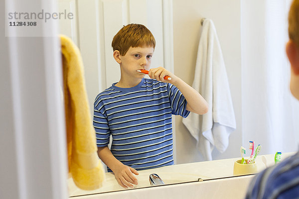 Reflexion eines kaukasischen Jungen beim Zähneputzen im Spiegel