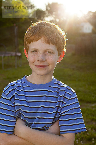 Lächelnder kaukasischer Junge im sonnigen Hinterhof stehend