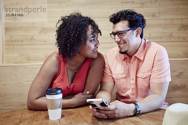 Lächelndes Paar  das in einem Café ein Mobiltelefon benutzt