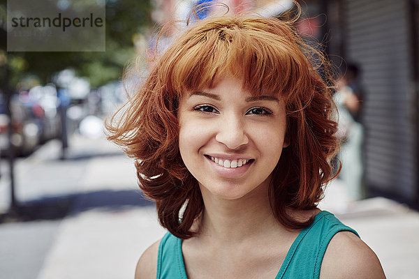 Lächelnde hispanische Frau auf dem Bürgersteig der Stadt
