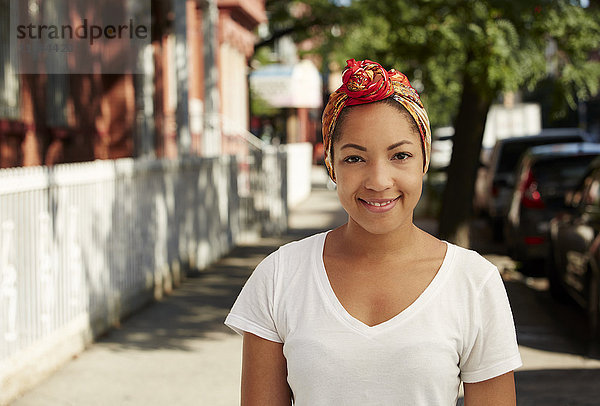 Porträt einer lächelnden schwarzen Frau mit Kopftuch auf dem Bürgersteig einer Stadt