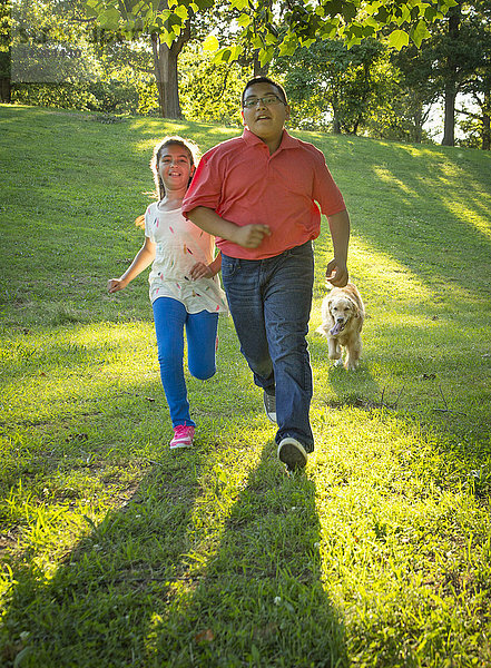 Hispanischer Bruder und Schwester laufen mit Hund auf einem Hügel