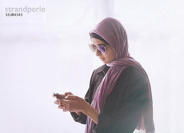 Mixed-Race-Mädchen mit herzförmiger Sonnenbrille und Kopftuch schreibt eine SMS