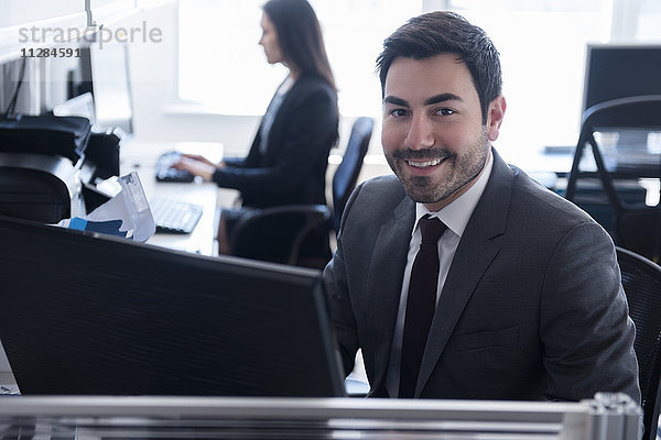 Porträt eines lächelnden Geschäftsmannes  der einen Computer im Büro benutzt