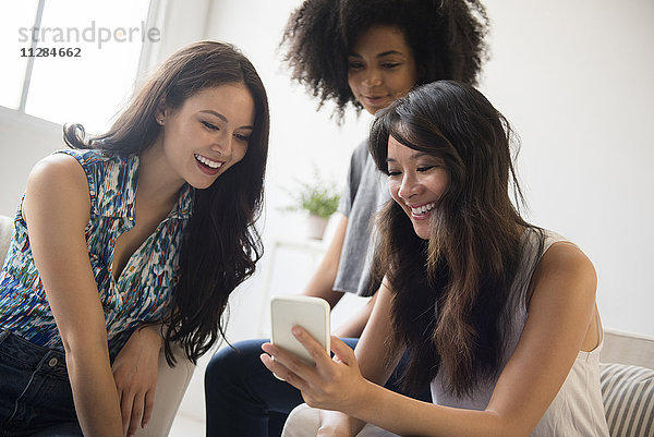 Lächelnde Frauen  die im Wohnzimmer eine SMS auf ihrem Handy schreiben