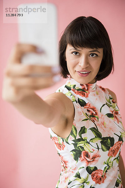 Hispanische Frau in geblümtem Kleid posiert für Handy-Selfie