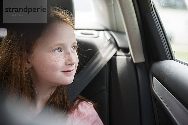Lächelndes kaukasisches Mädchen im Auto schaut aus dem Fenster