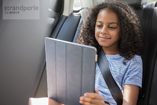 Lächelndes hispanisches Mädchen  das ein digitales Tablet im Auto benutzt