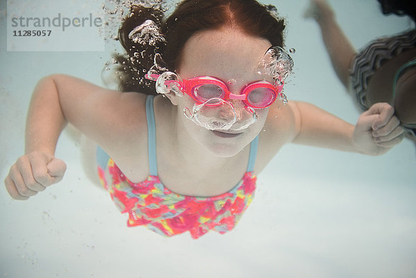 Mädchen schwimmt unter Wasser und trägt eine Schwimmbrille