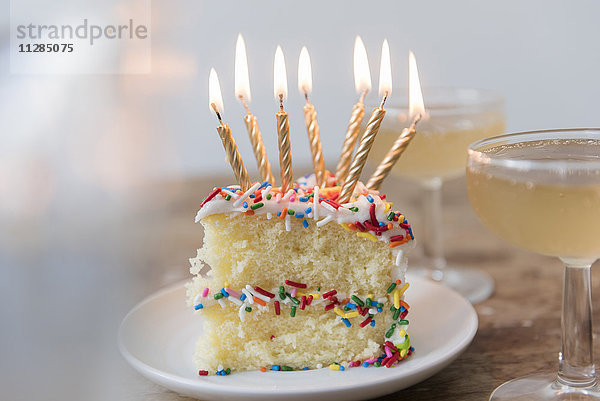 Kerzen brennen auf einem Stück Kuchen mit Streuseln in der Nähe von Champagner