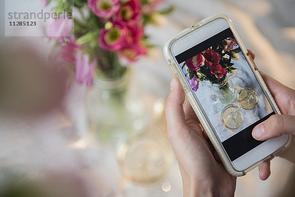 Kaukasische Frau fotografiert Champagner und Blumen mit dem Mobiltelefon