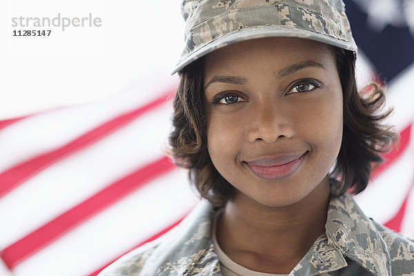 Porträt eines lächelnden gemischtrassigen Soldaten in der Nähe der amerikanischen Flagge